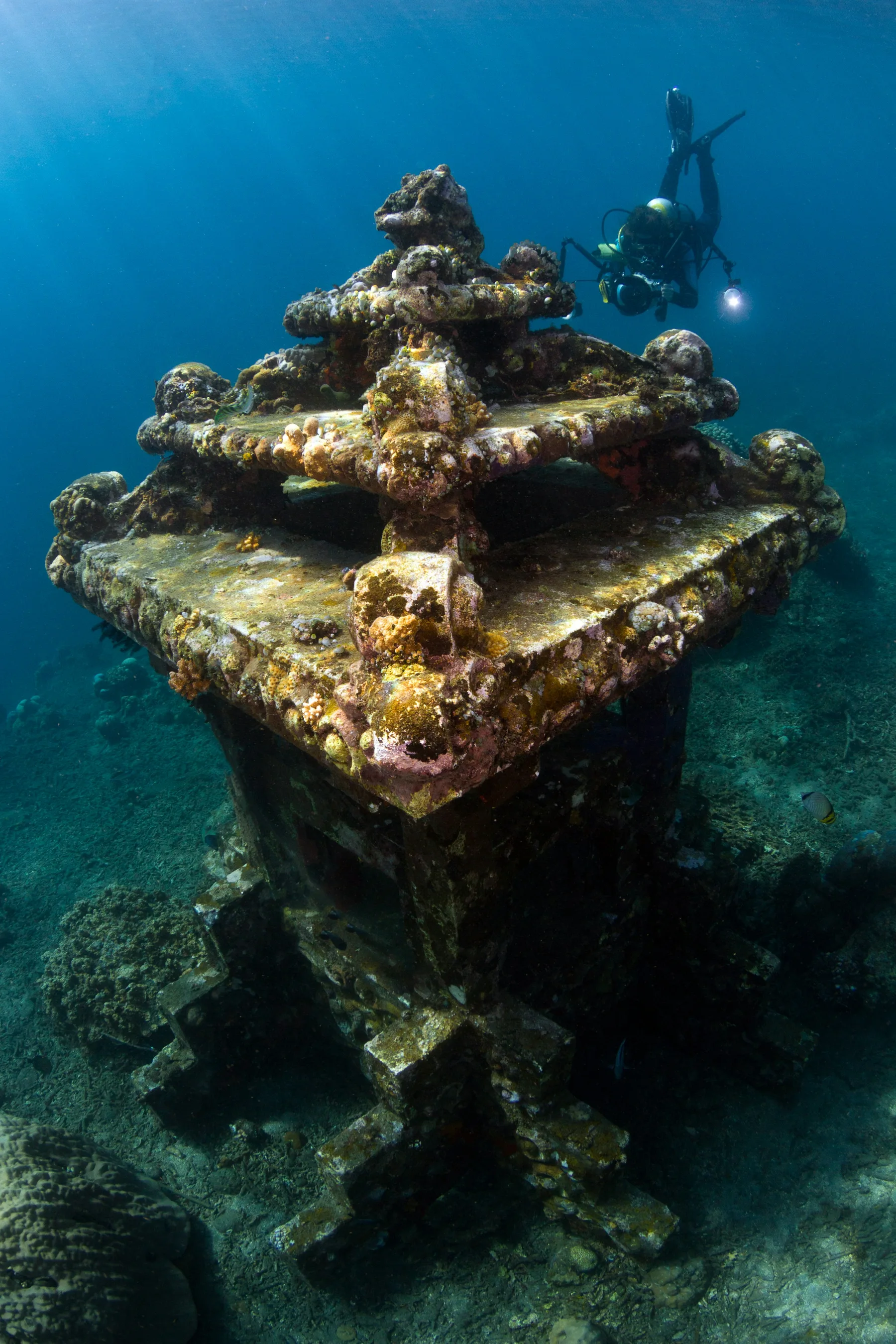 A scuba diver above a submerged Balinese sculpture at Amed.
